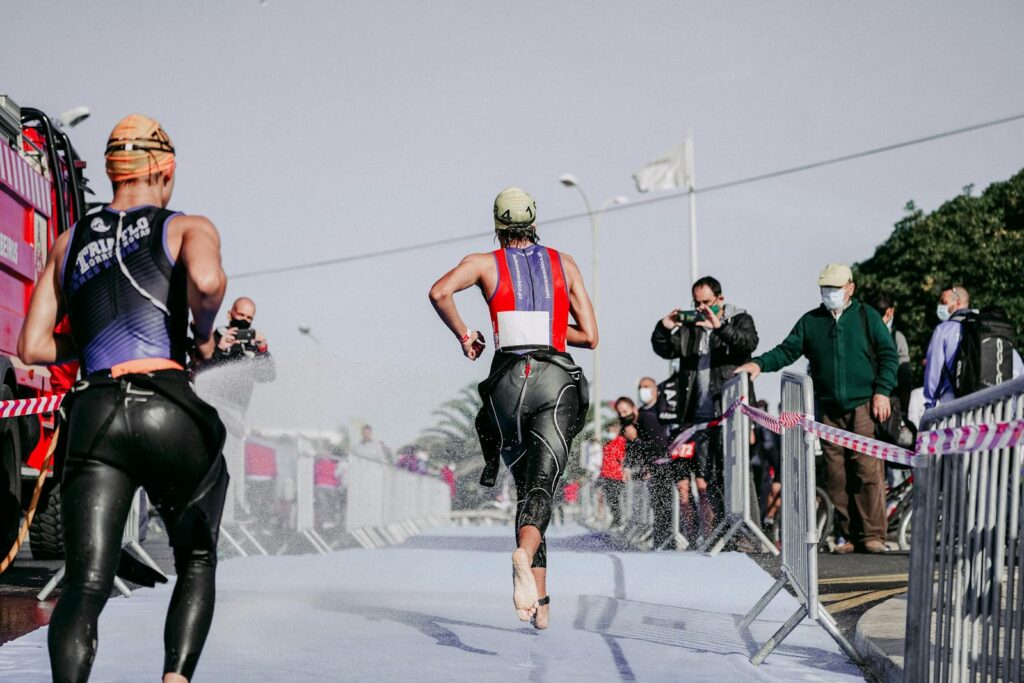 Back view of faceless group of people in wet sportswear running barefoot while taking part in competition