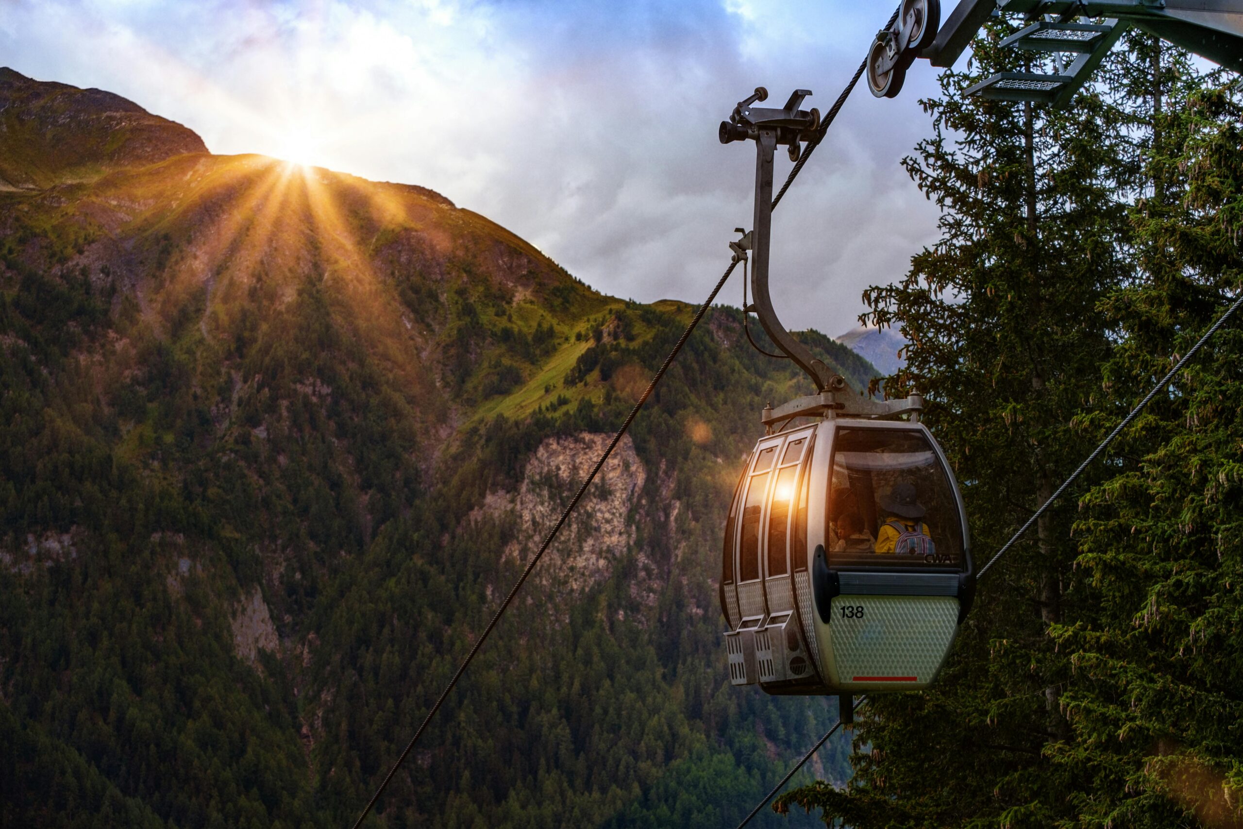 Photo by Bruno Glätsch Cable car in mountains with sunrise, green forests, and scenic landscape.